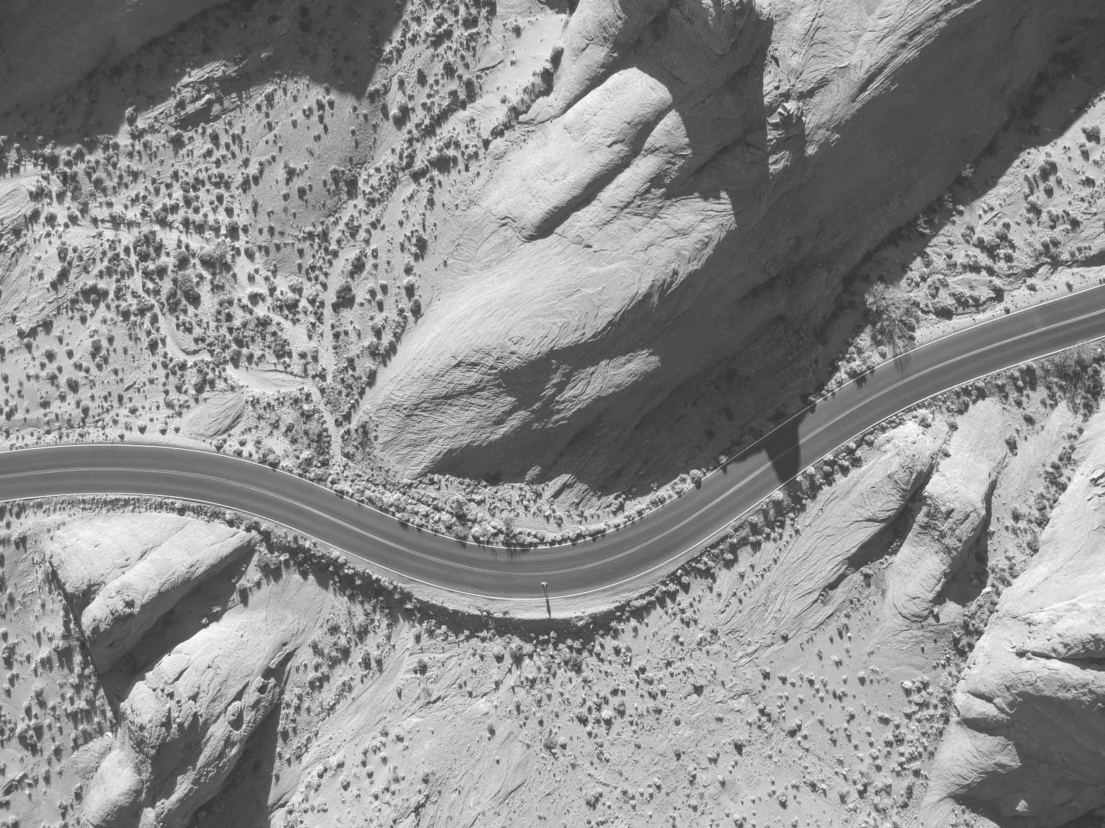 An aerial view of a winding desert road meandering between rugged mountains, highlighting the contrasting textures and patterns of the landscape and emphasizing the isolation and vastness of the desert terrain.